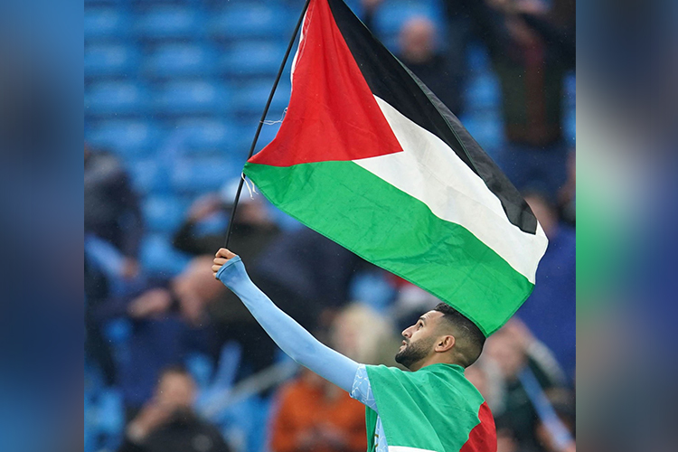 Manchester City footballer Riyad Mahrez carries the Palestinian flag on the pitch after their win against Everton